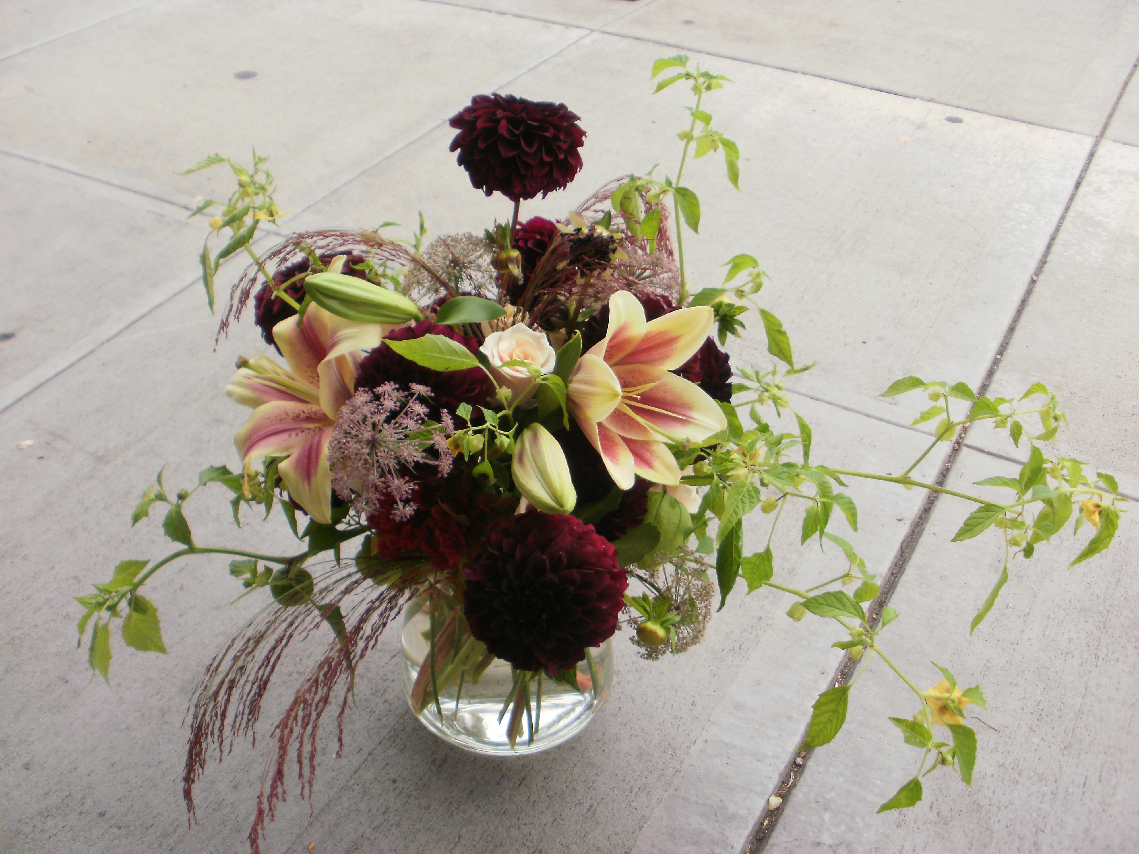 Low glass vase with burgundy dahlias and pink lilies with trailing greenery.