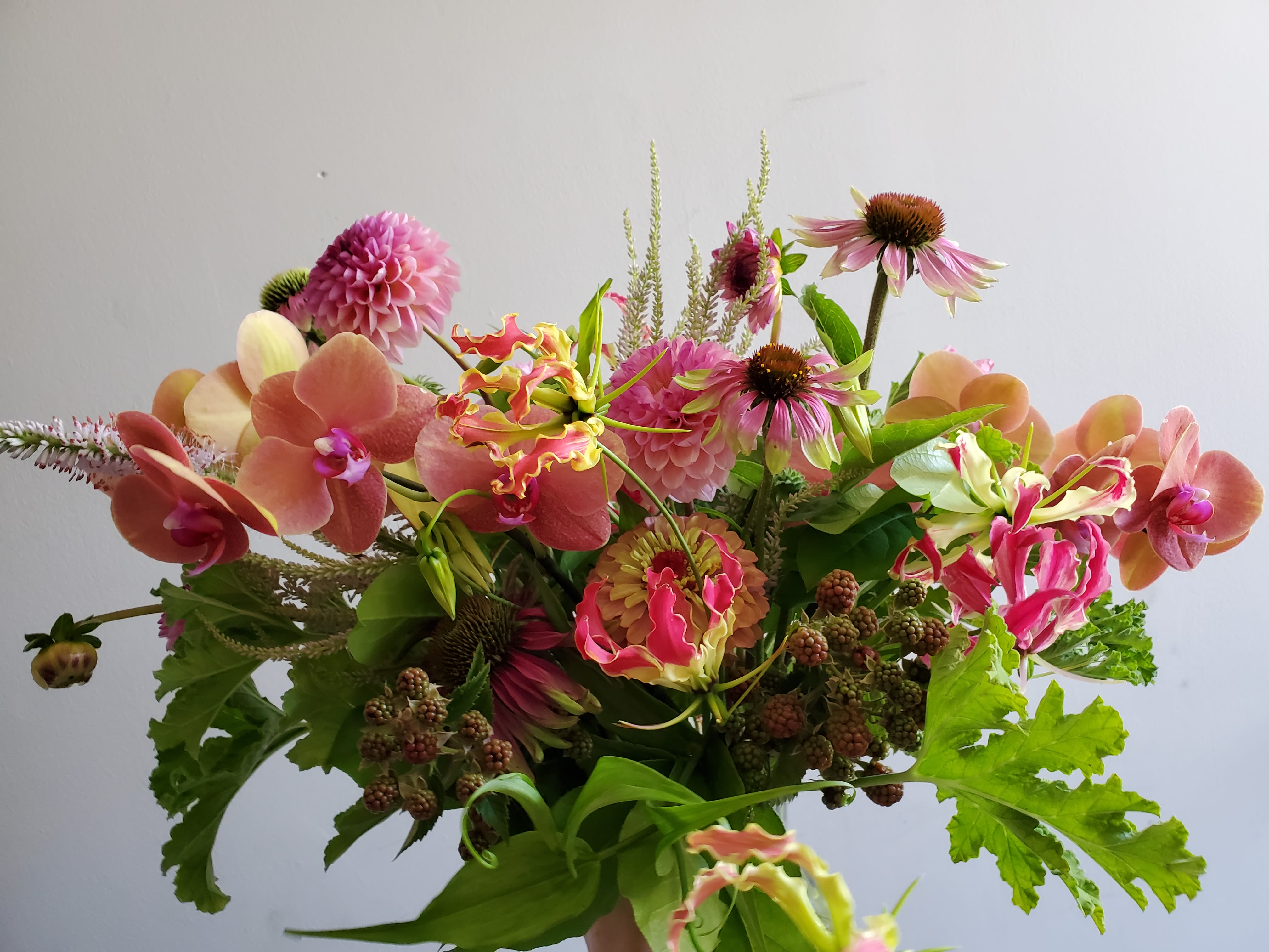 Loose bouquet of pink and peach orchids, dahlias, and mixed flowers with berries.