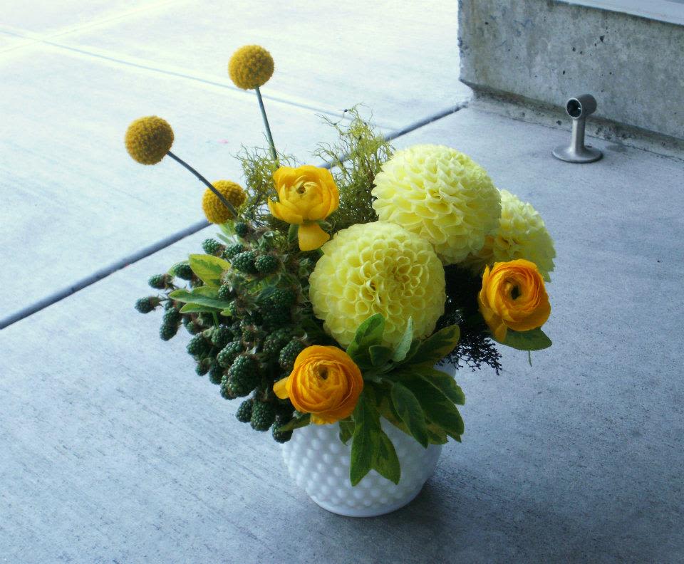 Low arrangement of yellow dahlias and ranunculus in a white vase on concrete