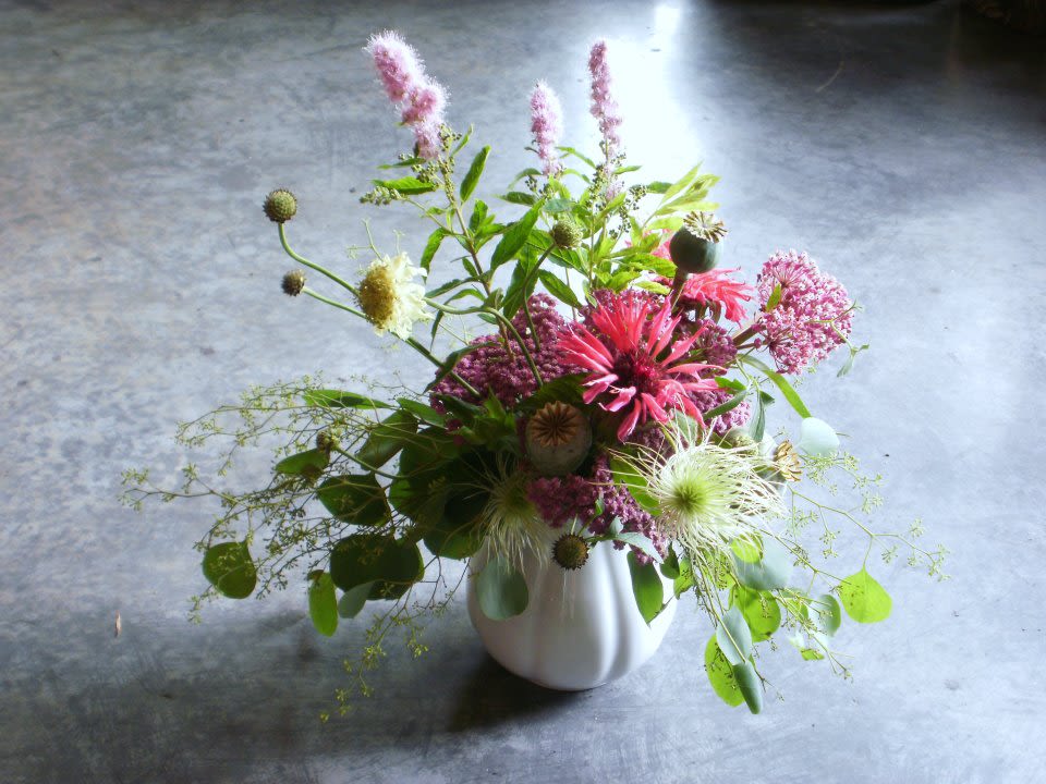 Loose garden-style arrangement of pink and white wildflowers in a white ceramic vase