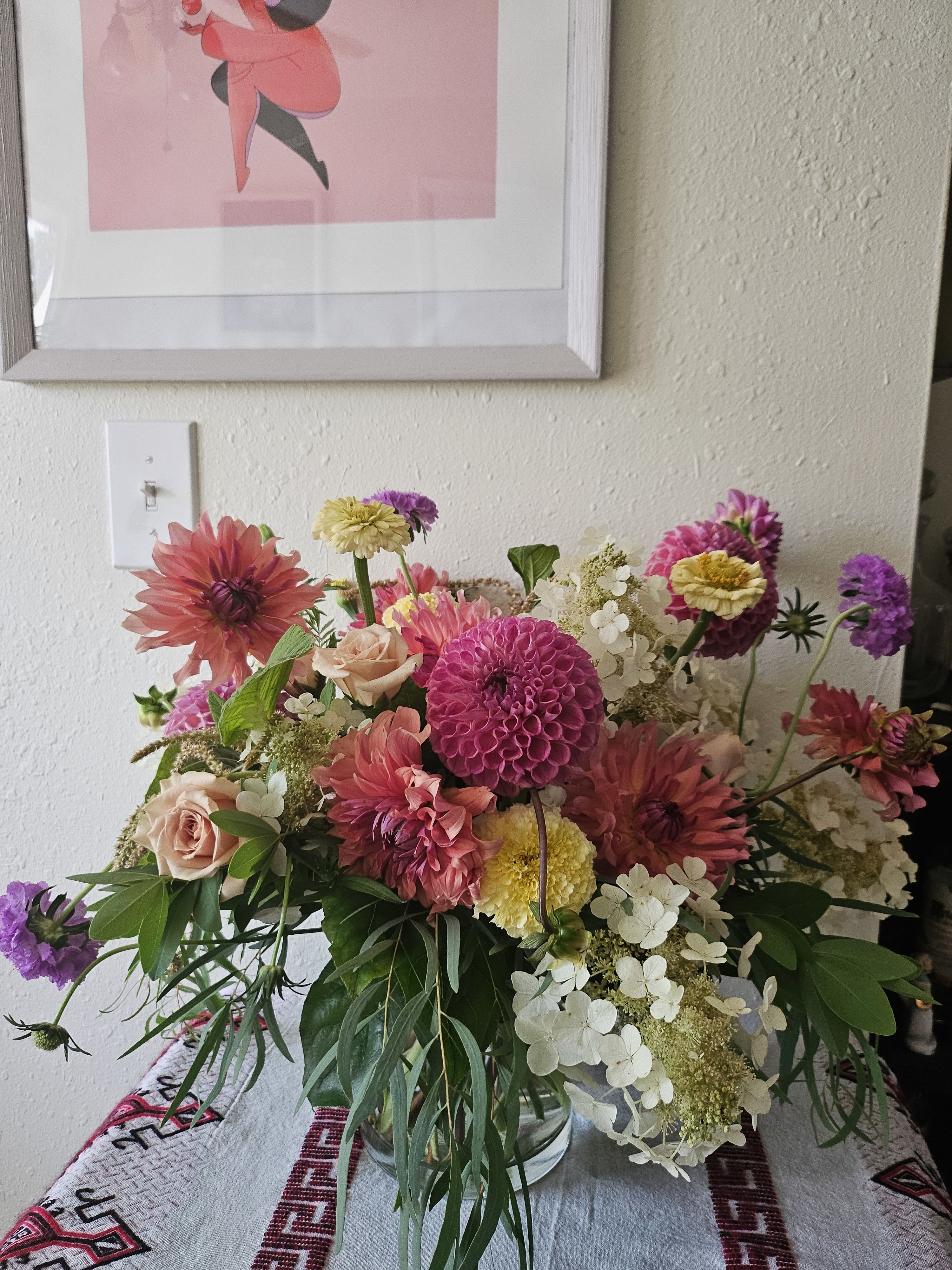 Loose garden-style arrangement of pink dahlias, roses, and white hydrangeas in a clear glass vase