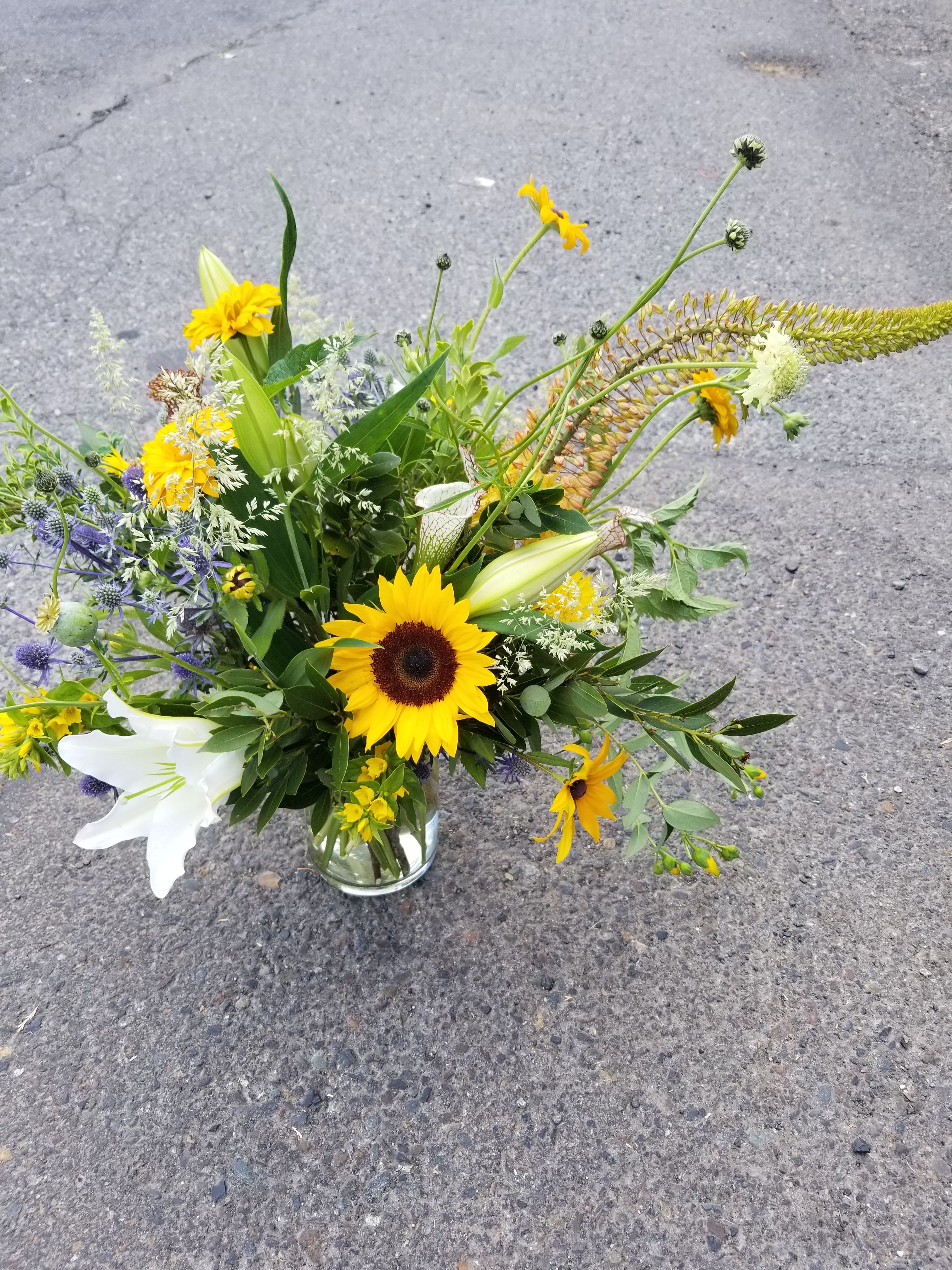 Loose mixed bouquet with sunflowers, white lilies and yellow daisies in a clear glass vase