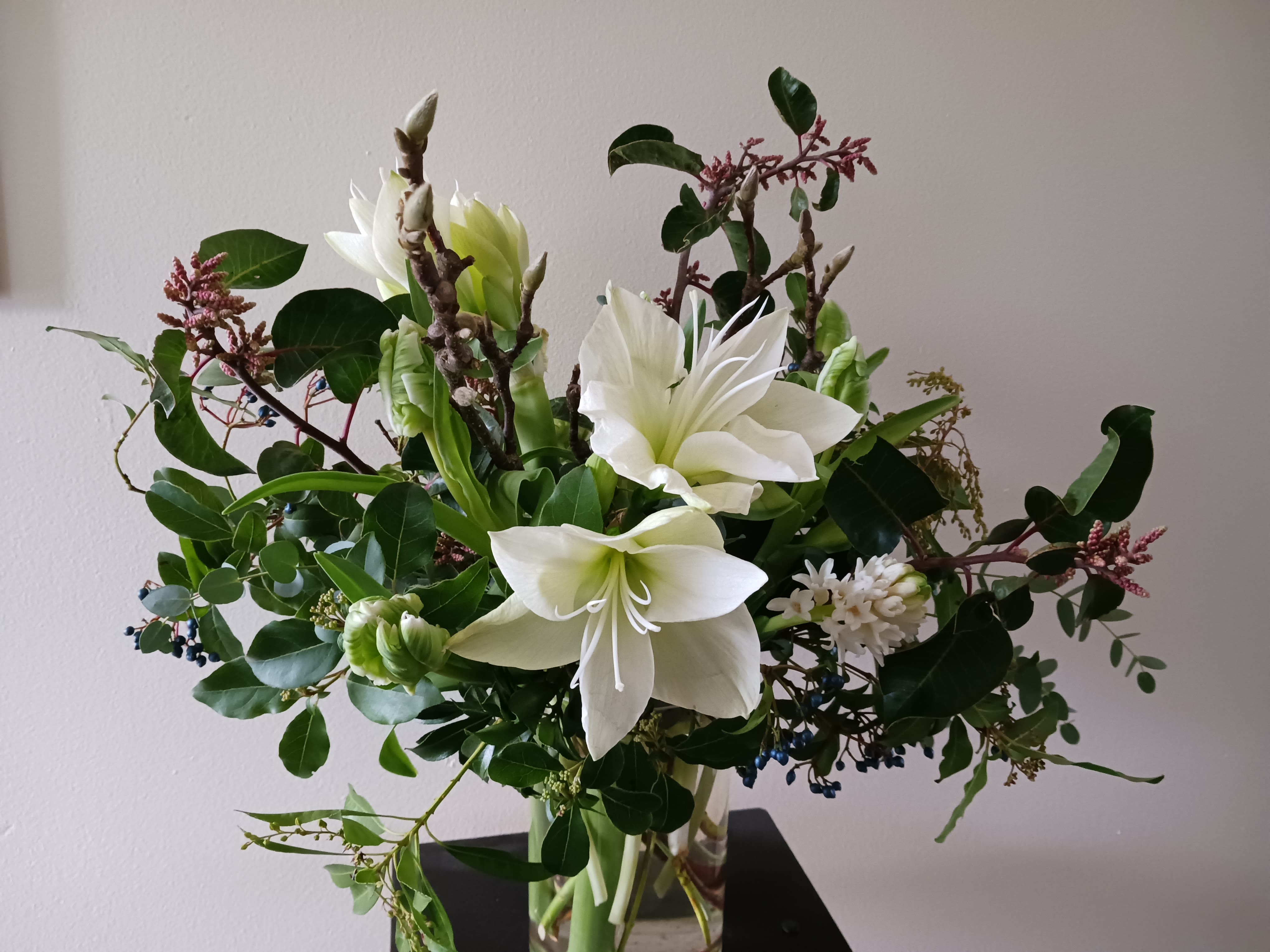 Tall arrangement of white amaryllis and other white blooms in a clear glass vase