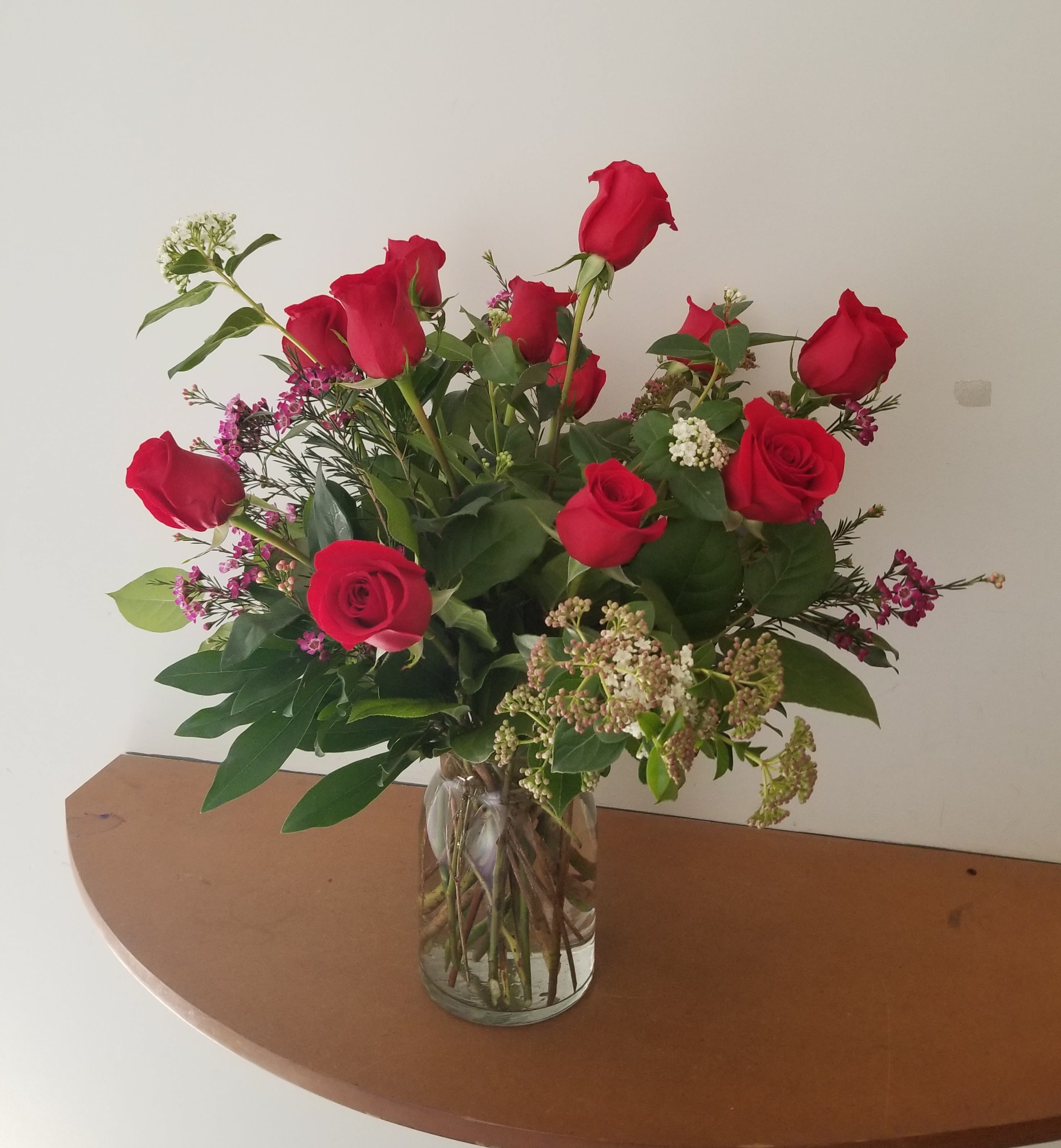 Arrangement of red roses with small white and pink filler flowers in a clear glass vase