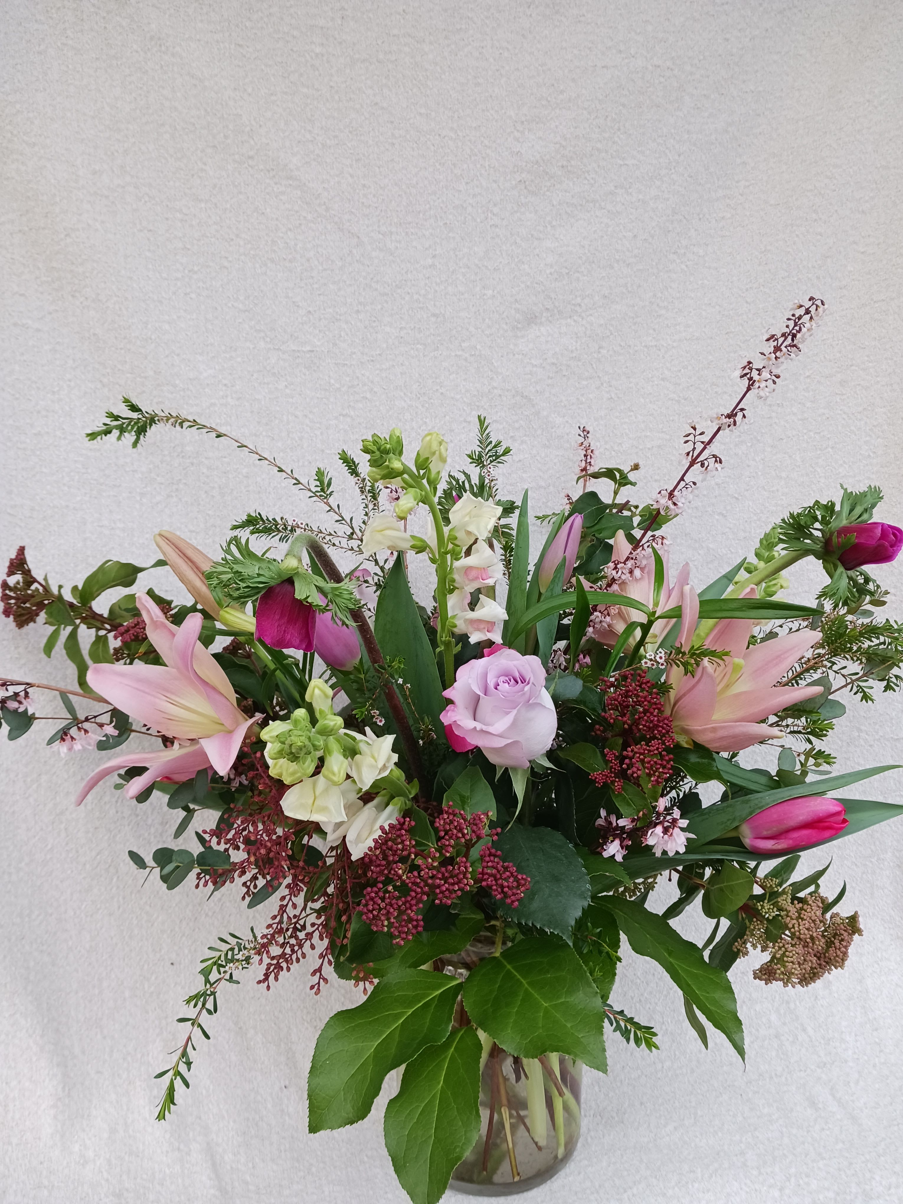 Tall arrangement of pink lilies, tulips, and a lavender rose in a clear glass vase