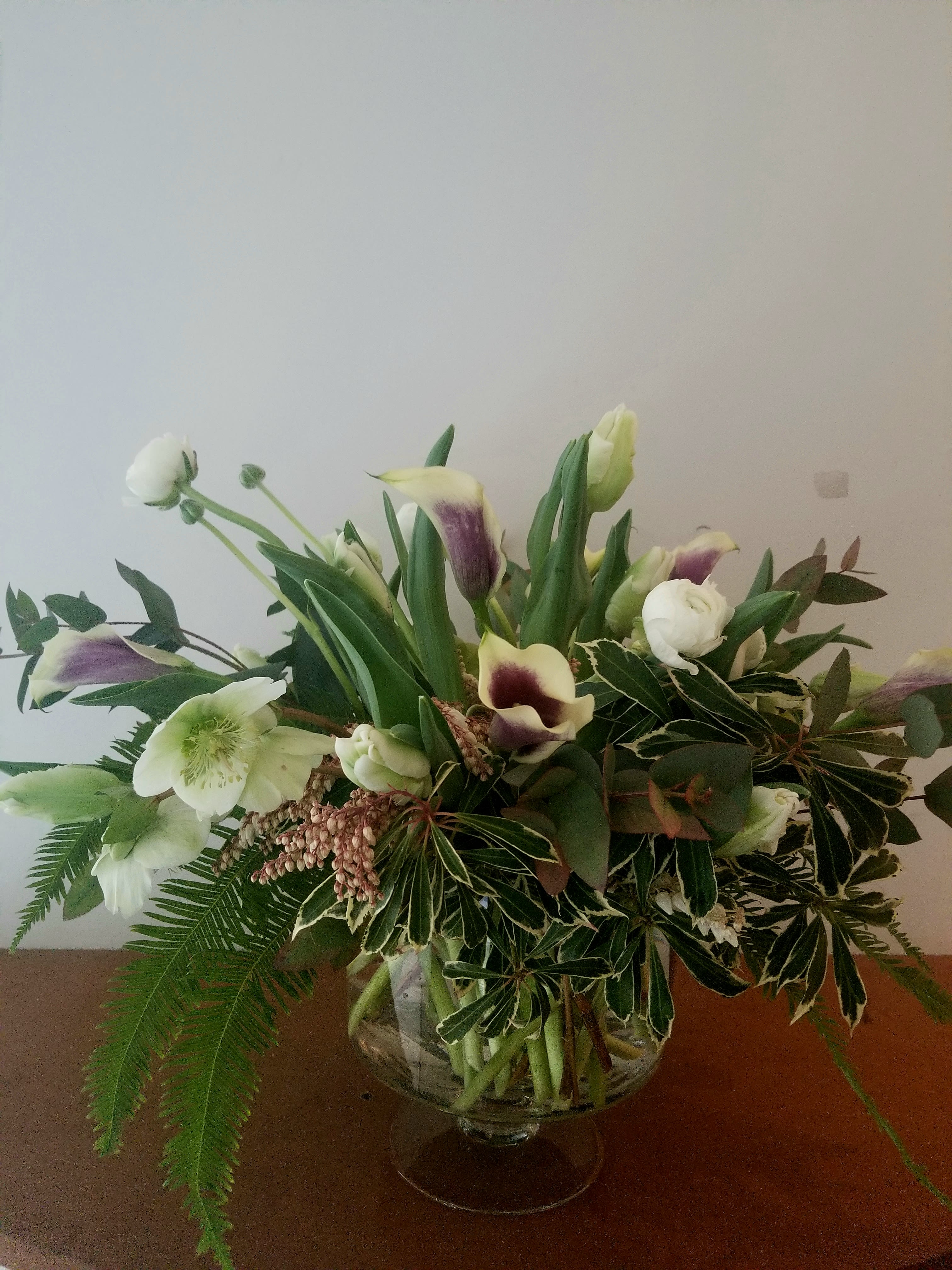 Low glass vase arrangement with white and purple calla lilies, white blooms, and abundant greenery.