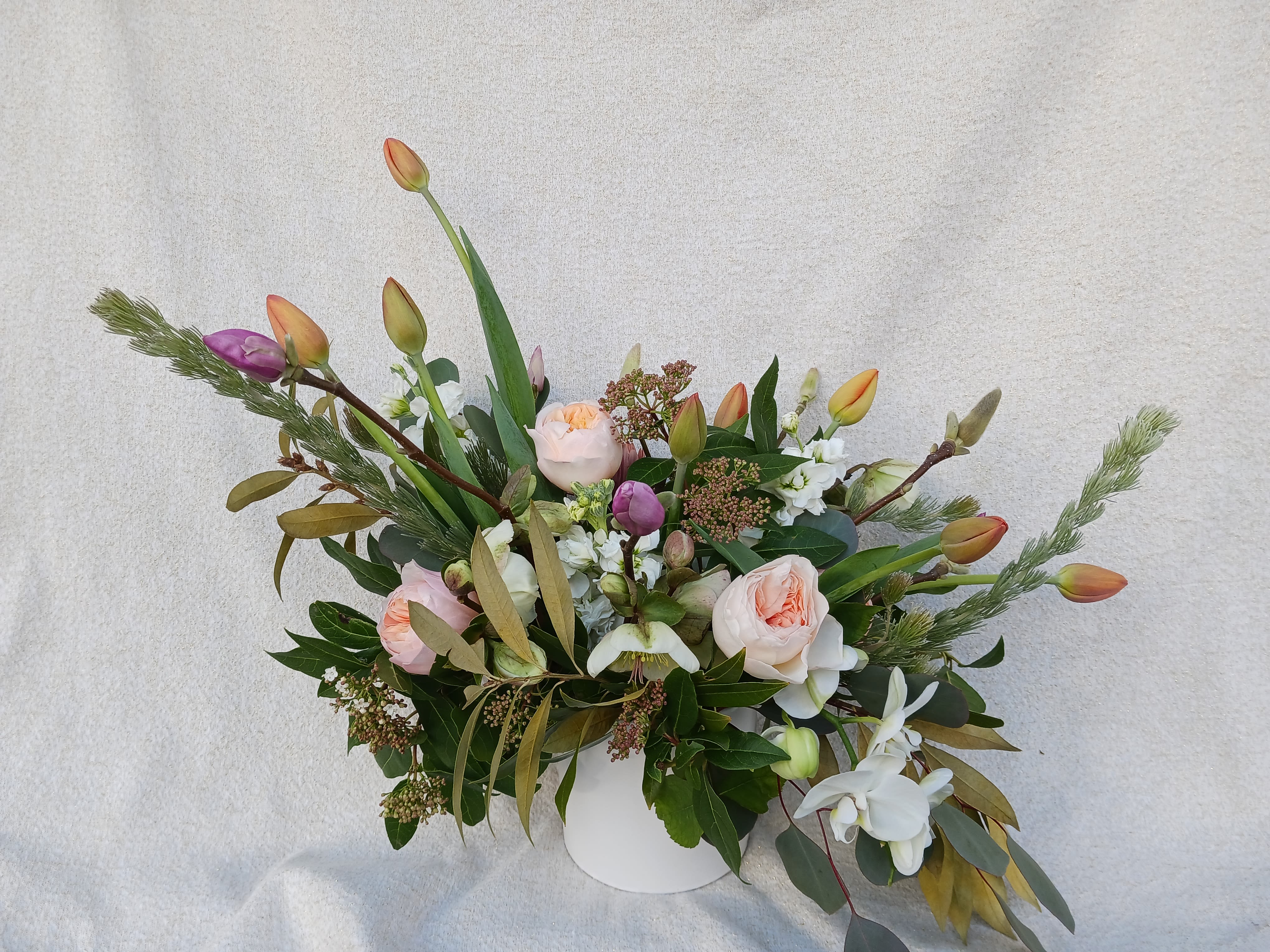 Wide peach rose and tulip arrangement with white orchids and stock in a white vase