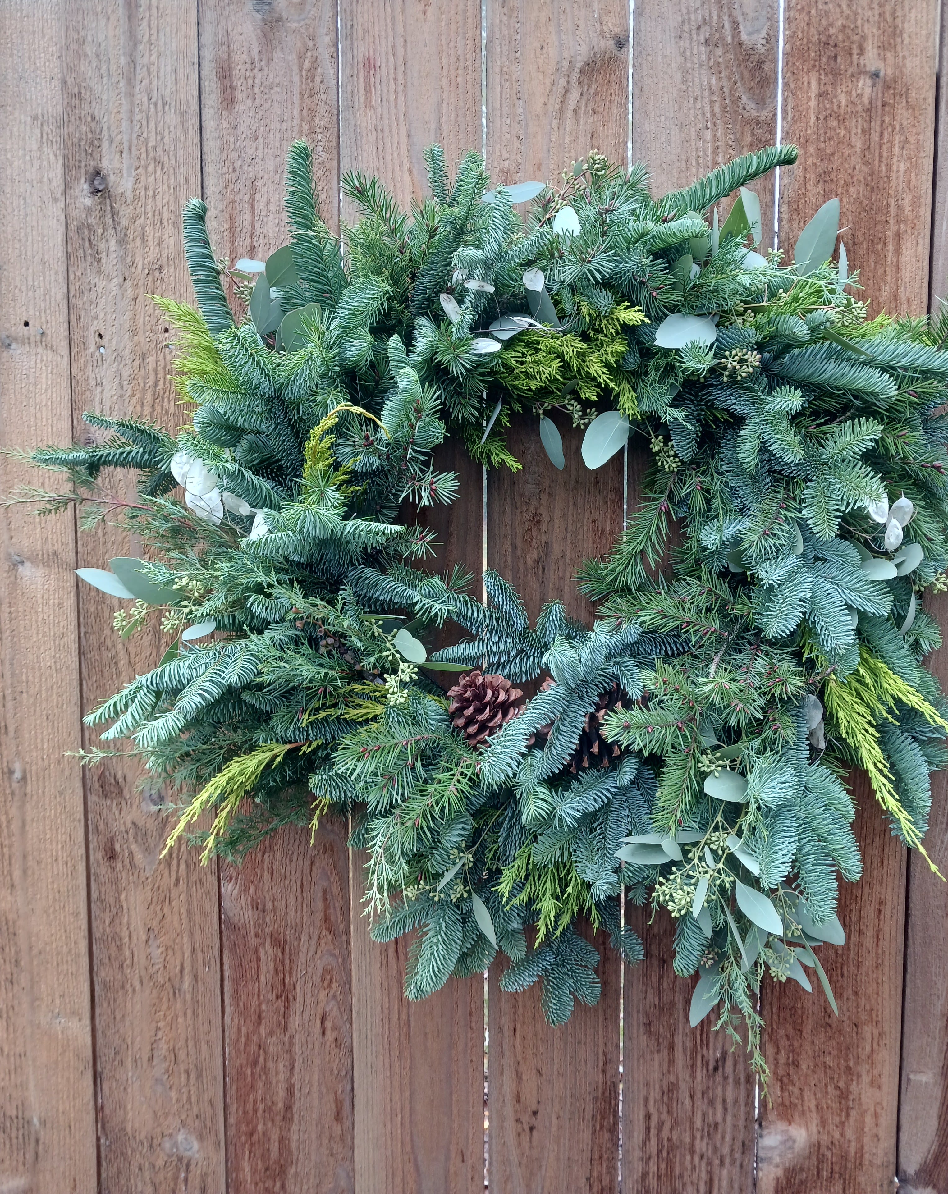 Evergreen wreath with pinecones and mixed foliage hanging on a wooden fence