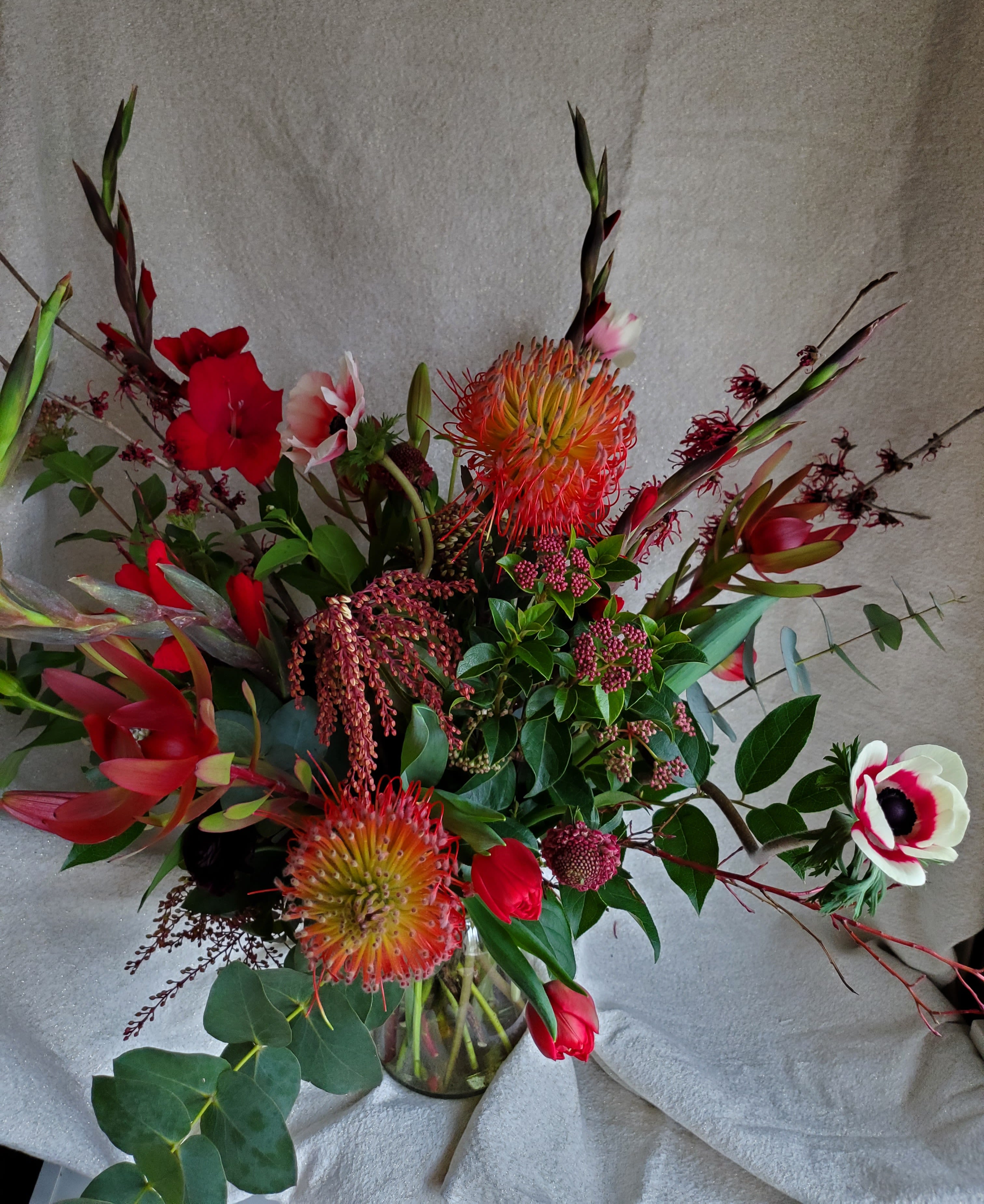 Tall red and white floral arrangement with pincushion protea in a clear glass vase.