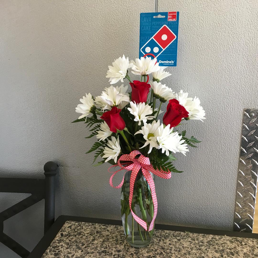 Red roses and white daisies in a clear glass vase with a checkered ribbon.