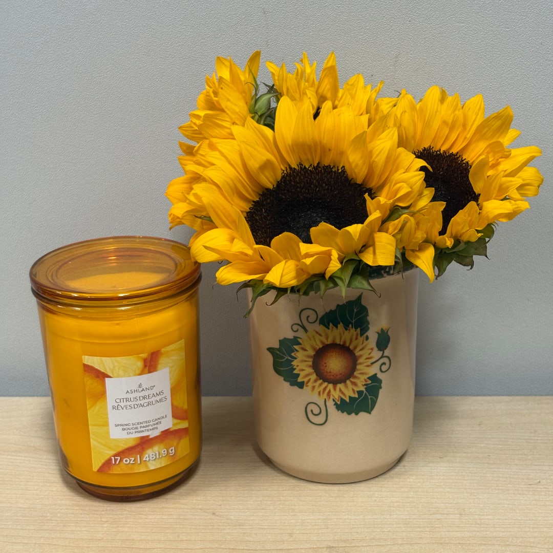 Sunflowers in a ceramic vase beside a yellow candle