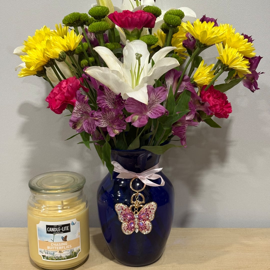 Mixed bouquet in a blue vase with a butterfly charm, beside a candle jar