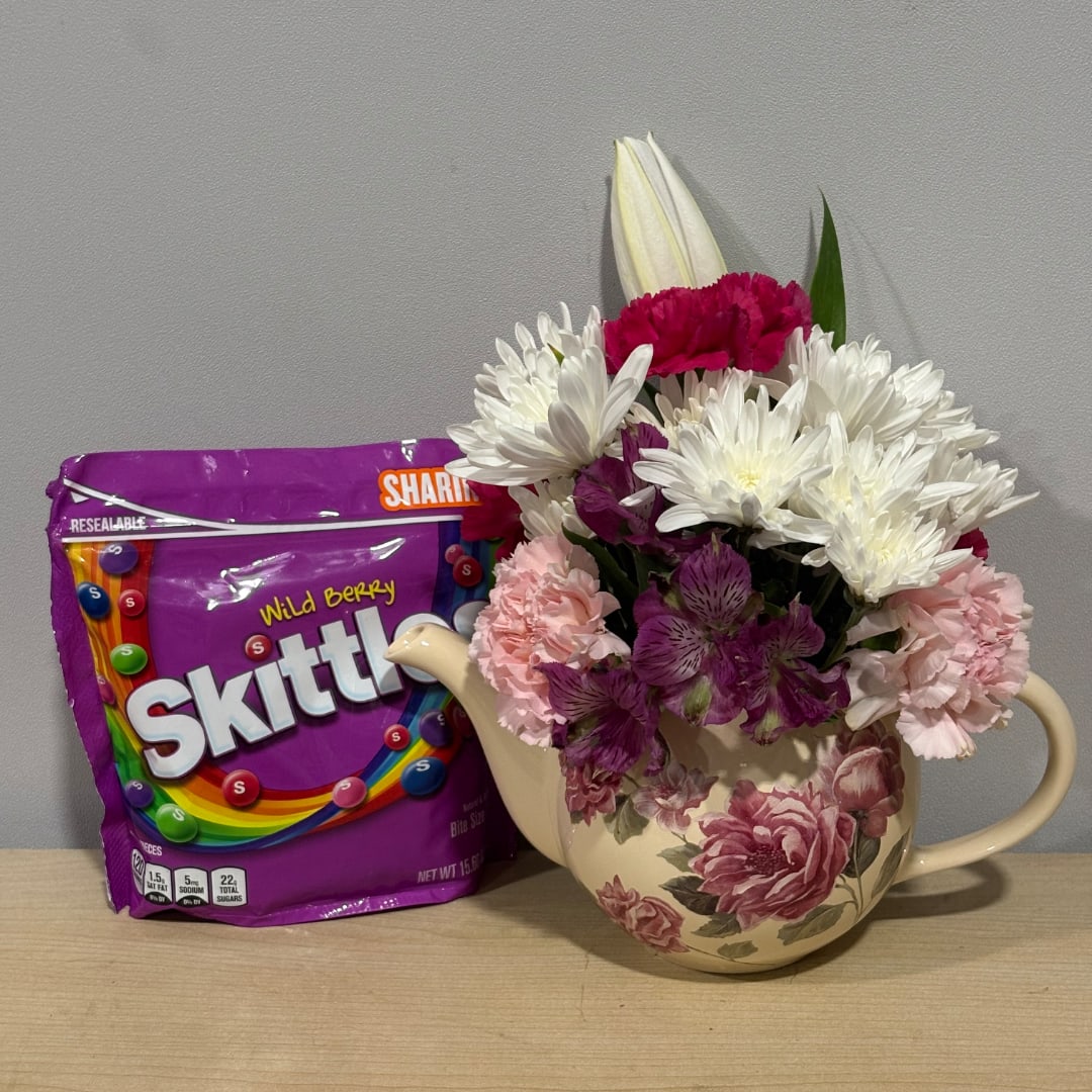 Mixed bouquet in a floral teapot vase beside a purple Skittles bag