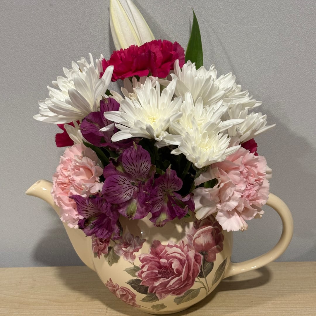 Mixed bouquet of white, pink, and purple flowers in a cream teapot vase