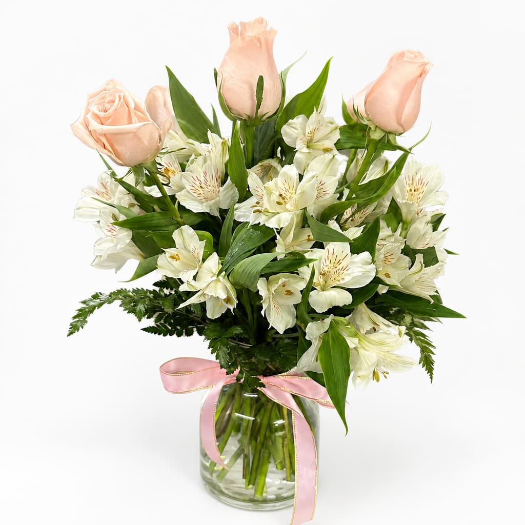 Peach roses and white alstroemeria in a glass vase with a pink ribbon