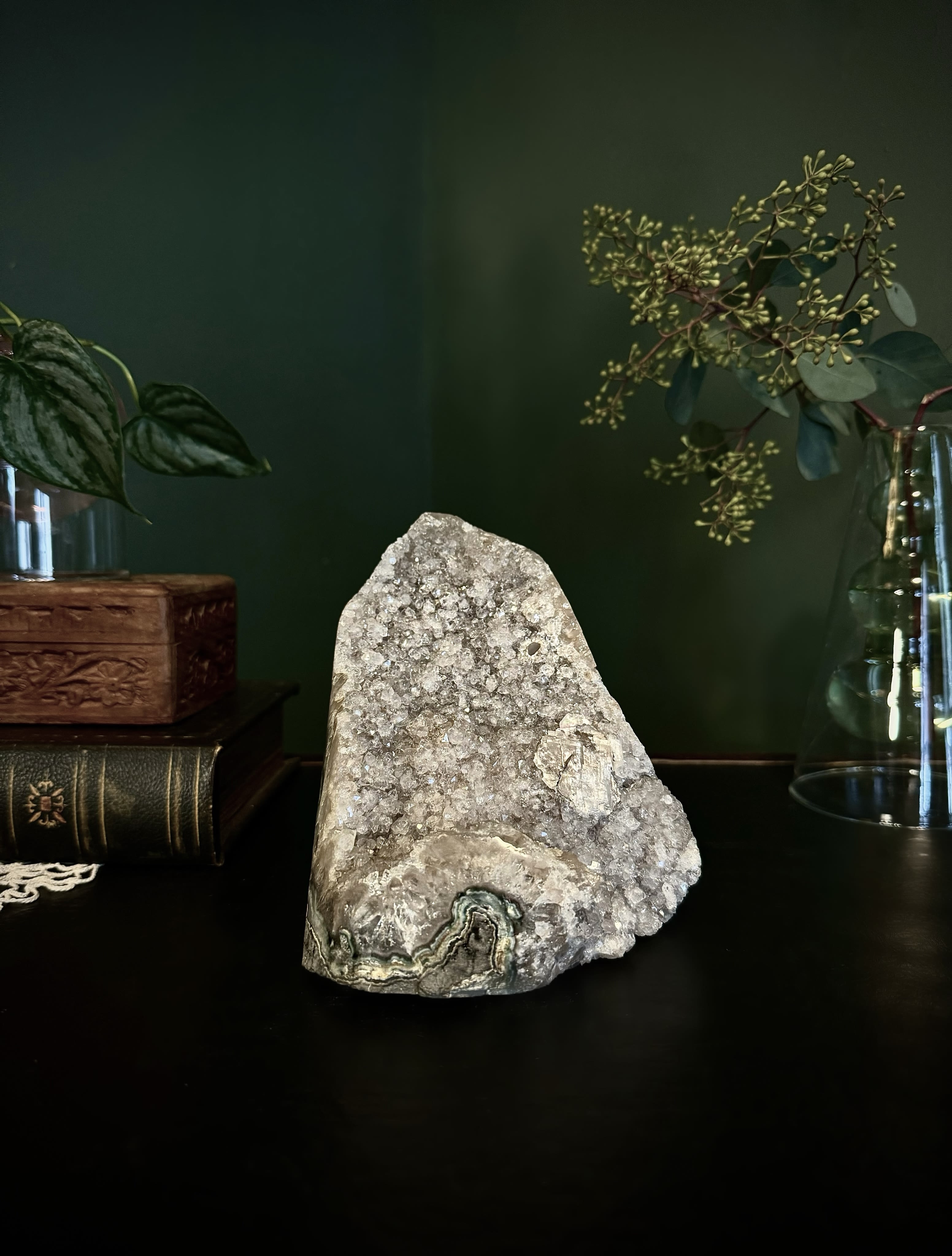 Crystal geode on a dark surface with glass vases and greenery