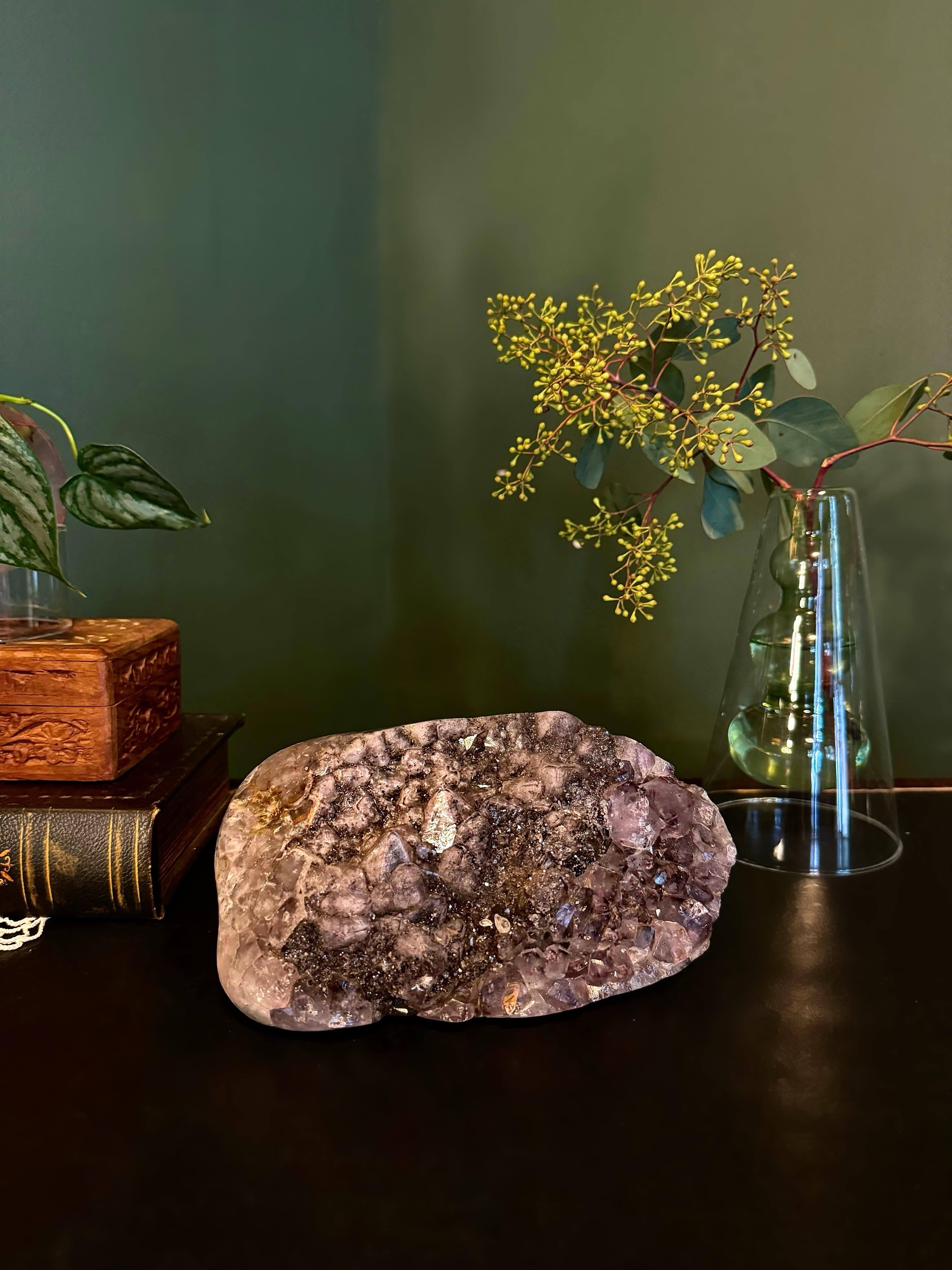 Amethyst crystal cluster on a dark surface beside a glass vase with branches