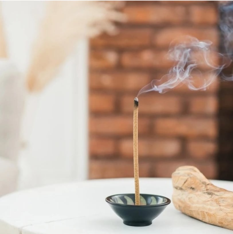 Lit incense stick in a small bowl with smoke rising