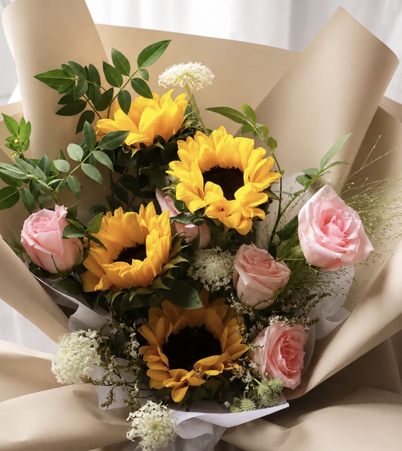 Bouquet of sunflowers and pink roses wrapped in beige paper
