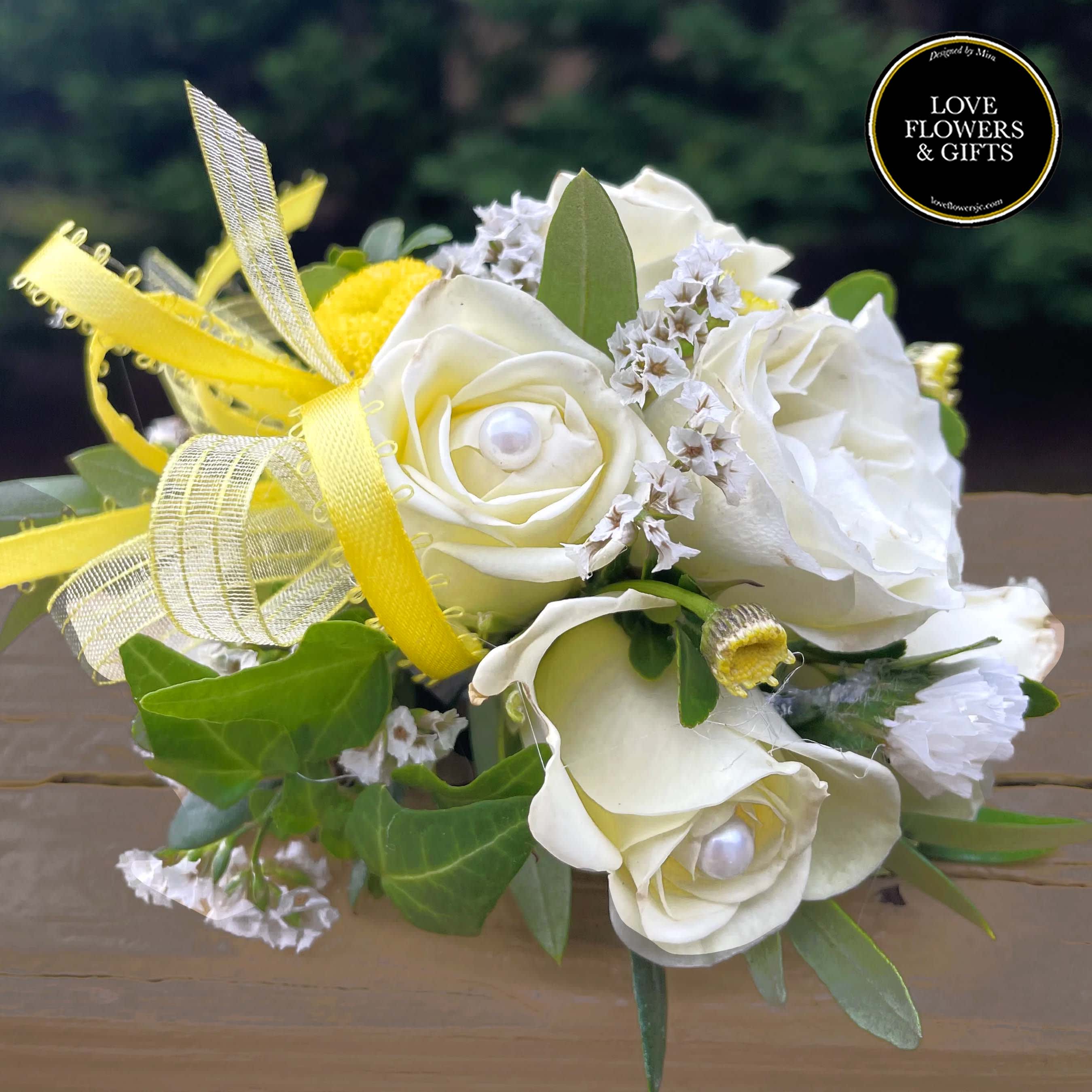 White rose corsage with yellow ribbon, pearl centers, and small white filler flowers