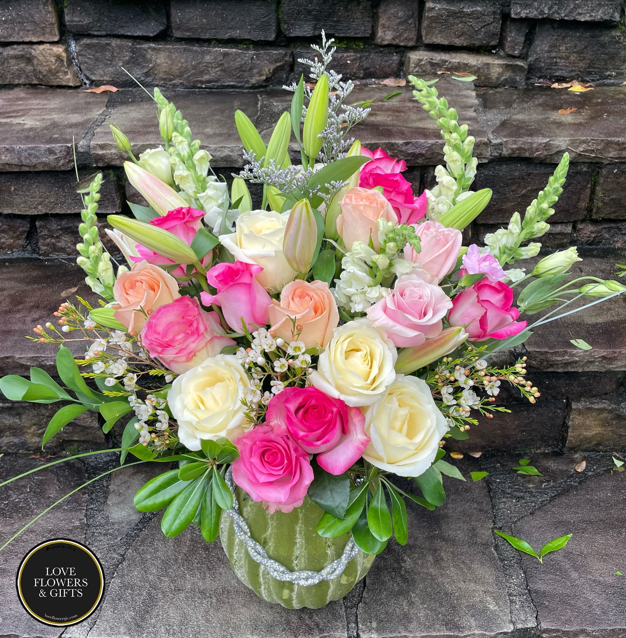 Mixed bouquet of pink, peach, and cream roses with lilies and snapdragons in a green vase