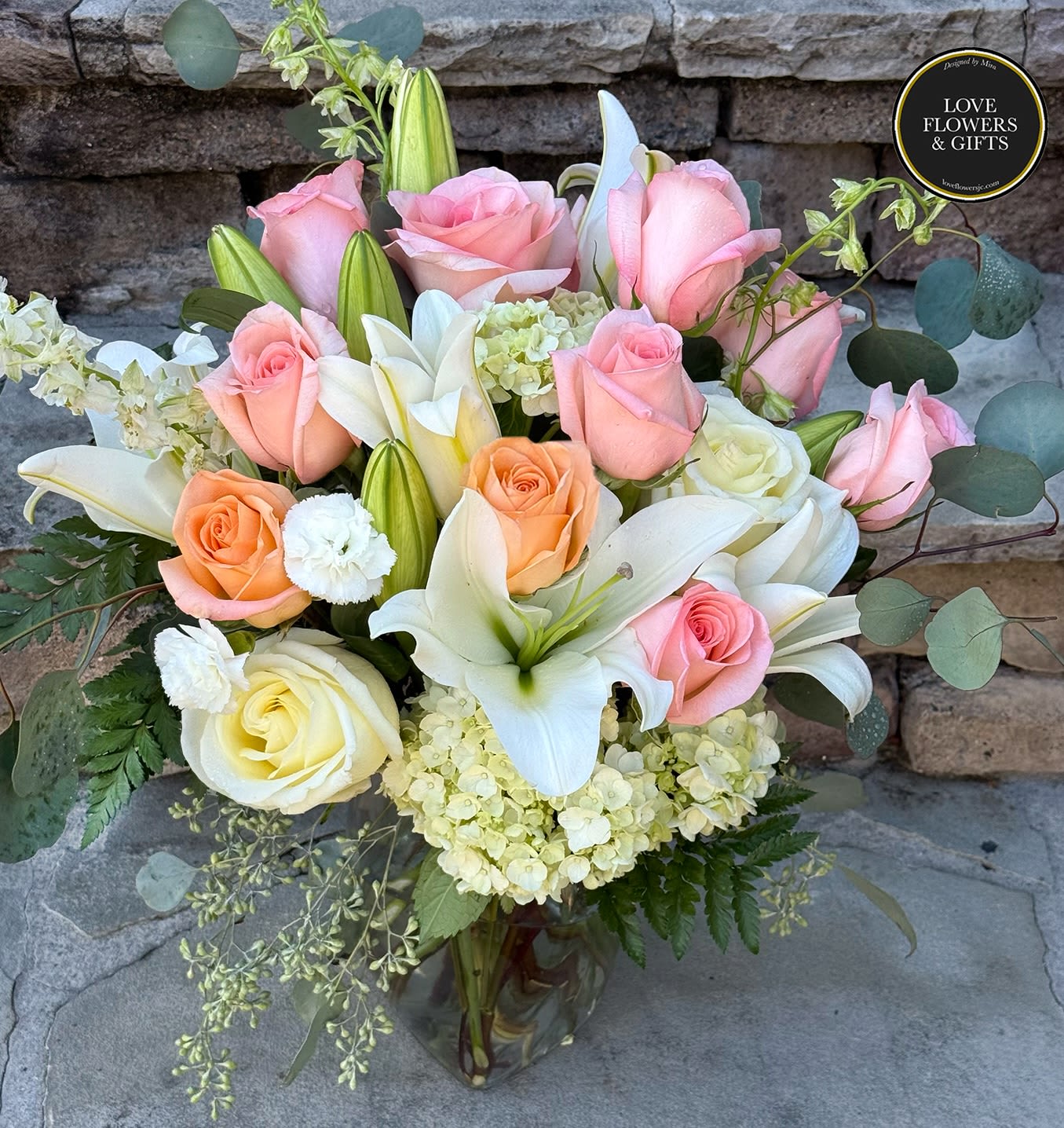 Glass vase arrangement of pink and peach roses with white lilies and hydrangea