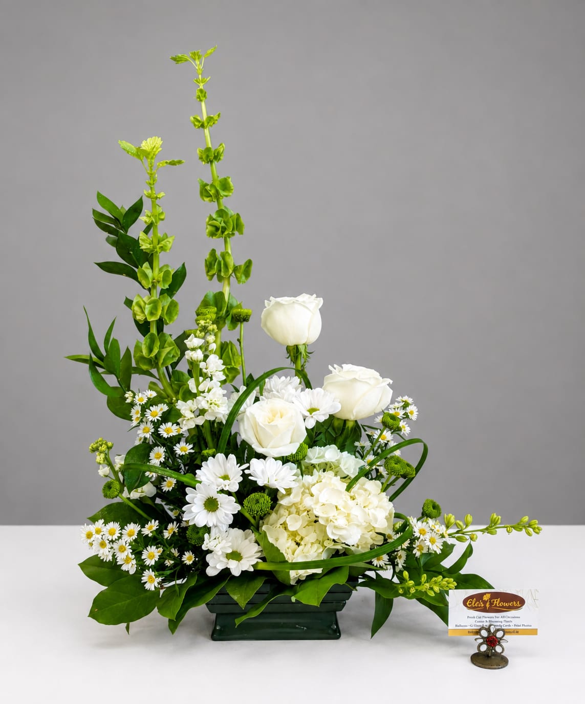 White roses and daisies arranged in a low green container with tall green spikes