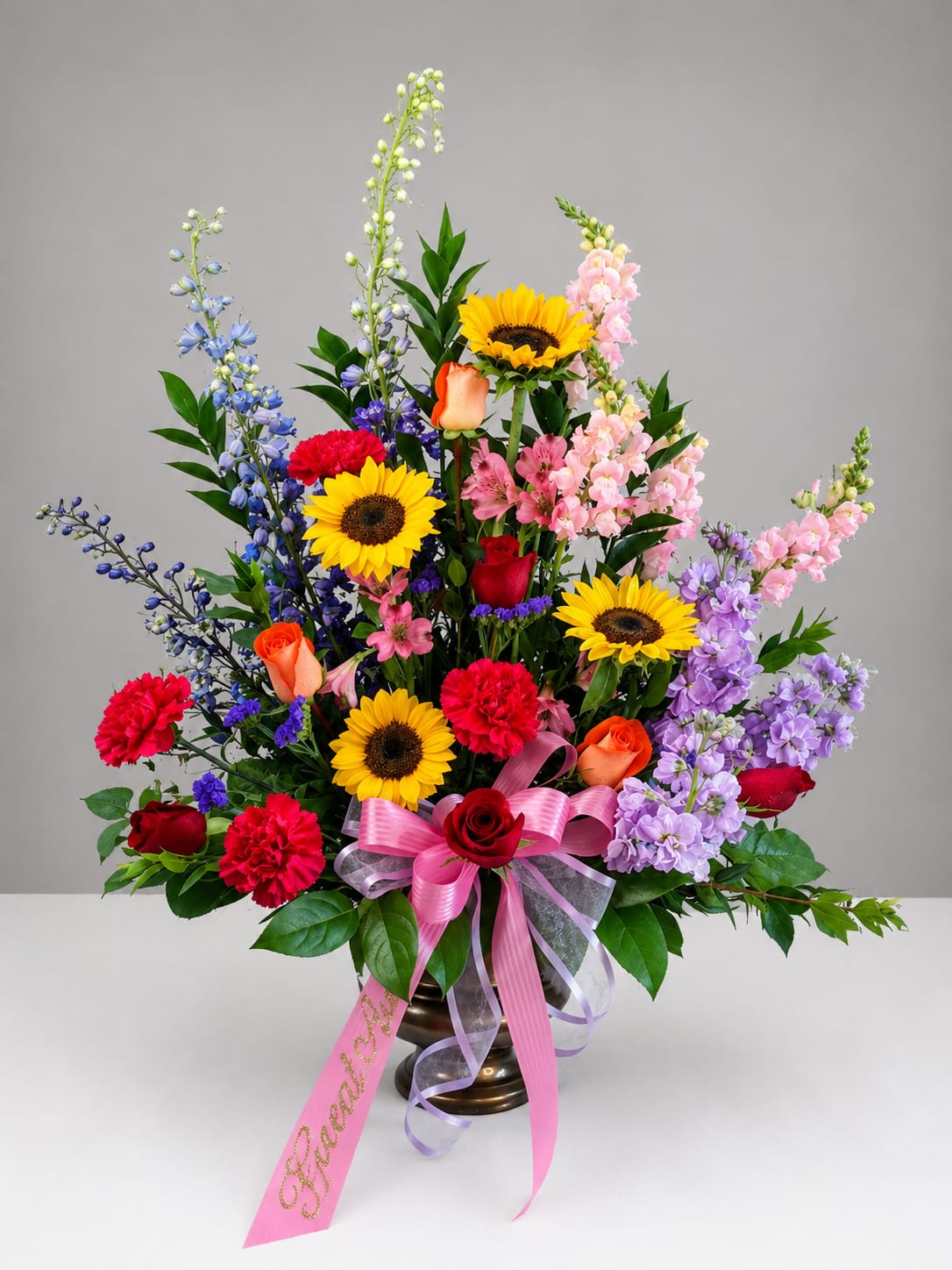 Colorful mixed flower arrangement in a bronze vase with a pink ribbon