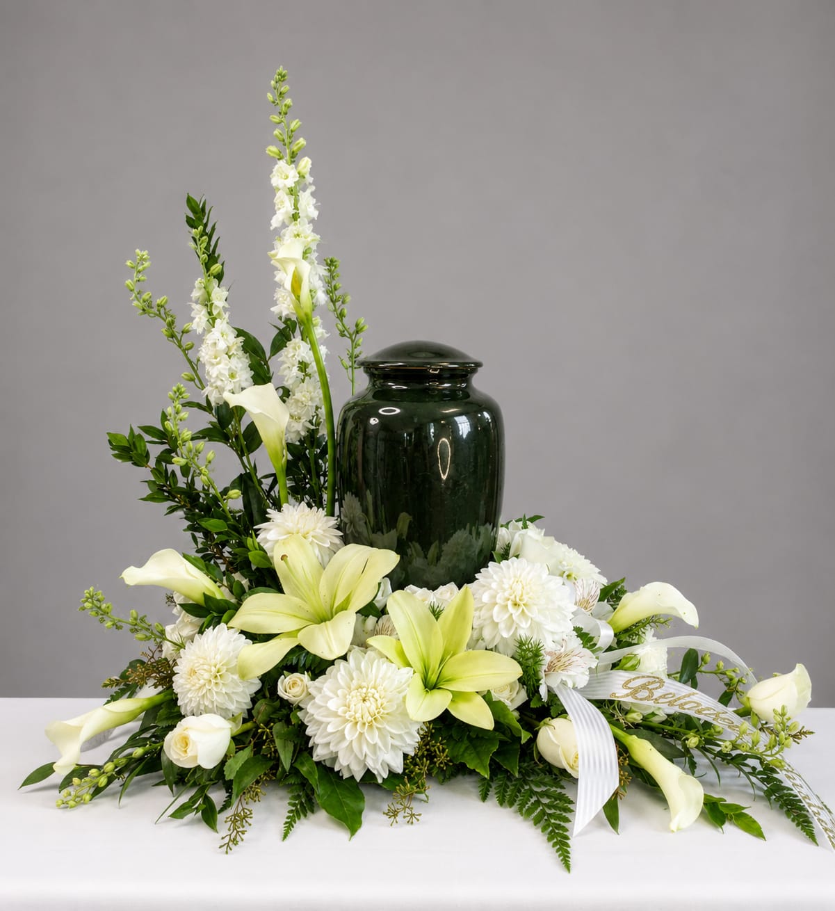 White lilies and mums arranged around a dark green urn