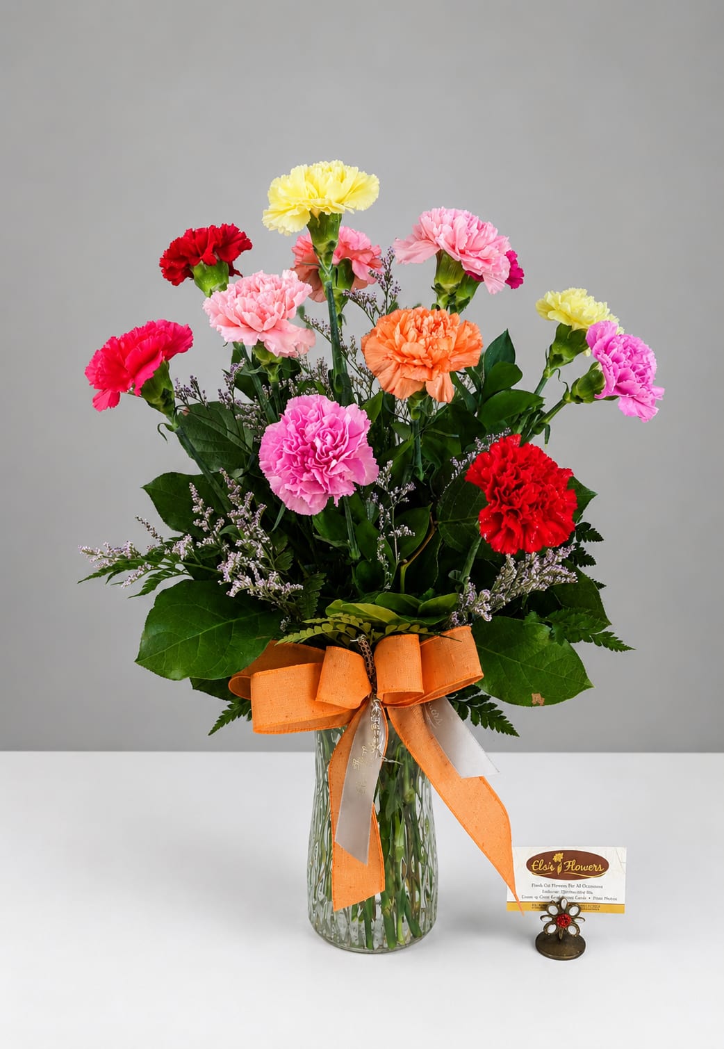 Colorful carnation bouquet in a glass vase with an orange ribbon