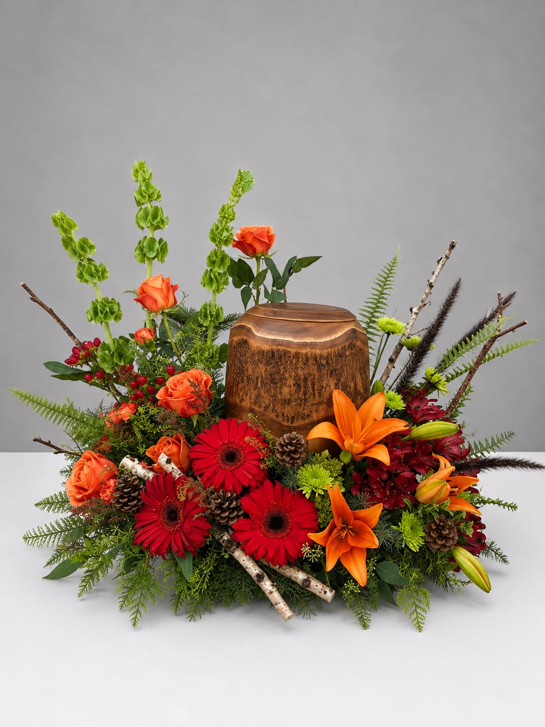 Autumn floral arrangement with orange roses, red gerberas, lilies, and a wooden urn