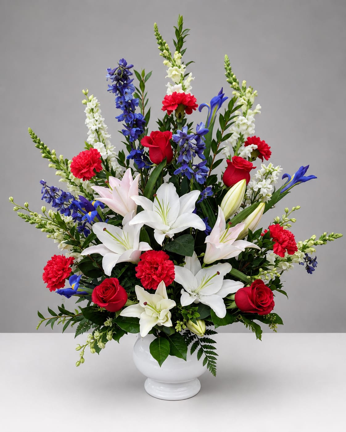 Large mixed bouquet in a white vase with red, white, blue, and pink flowers.