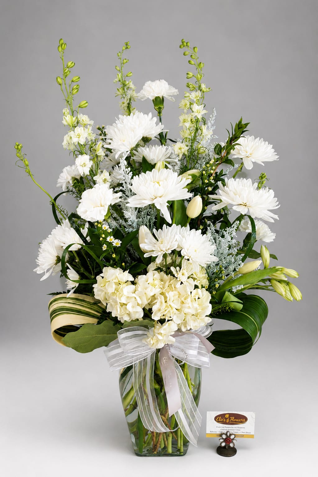 White floral arrangement in a glass vase with a ribbon bow