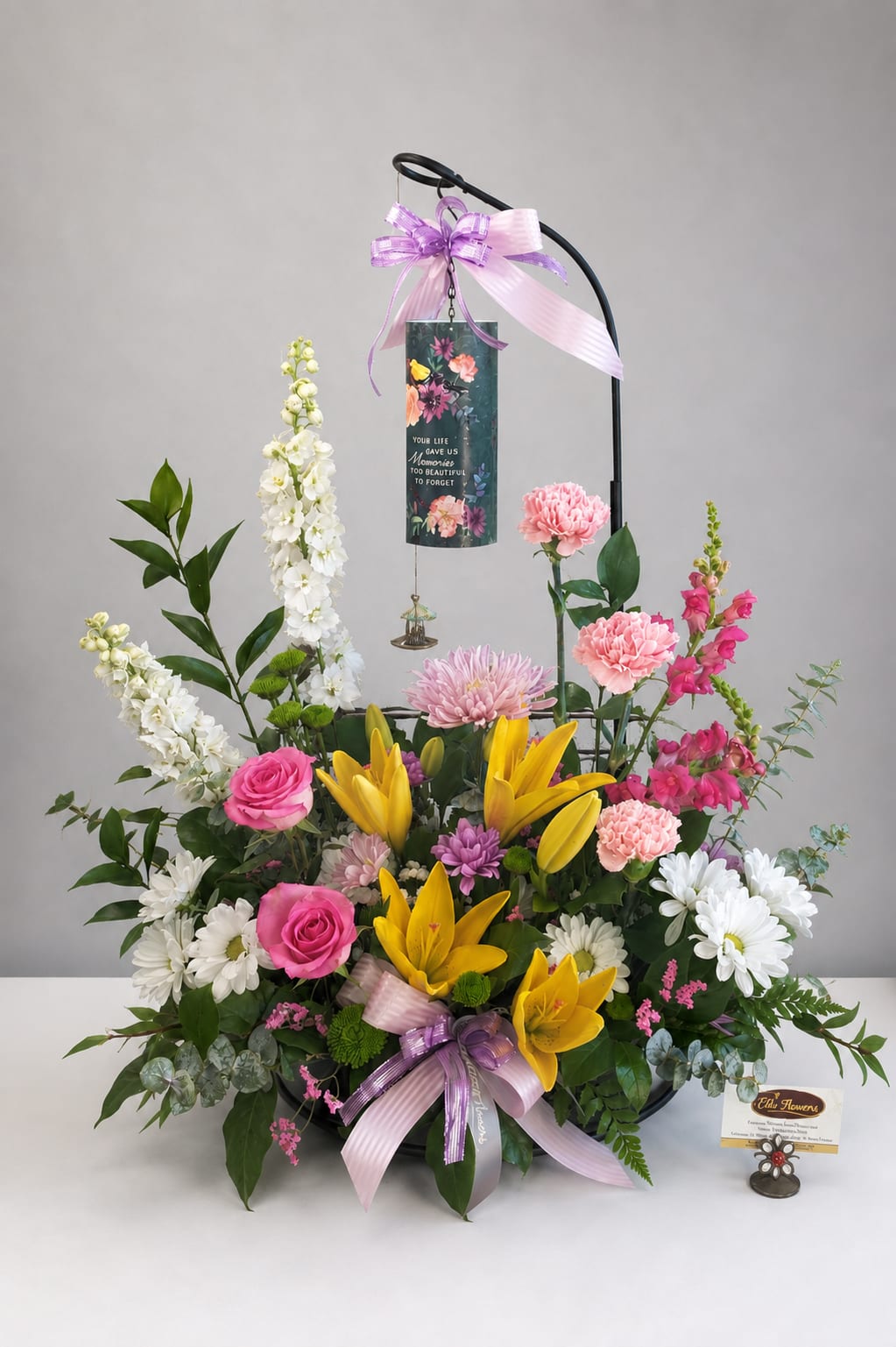 Standing floral sympathy arrangement with lilies, roses, and daisies on a black easel
