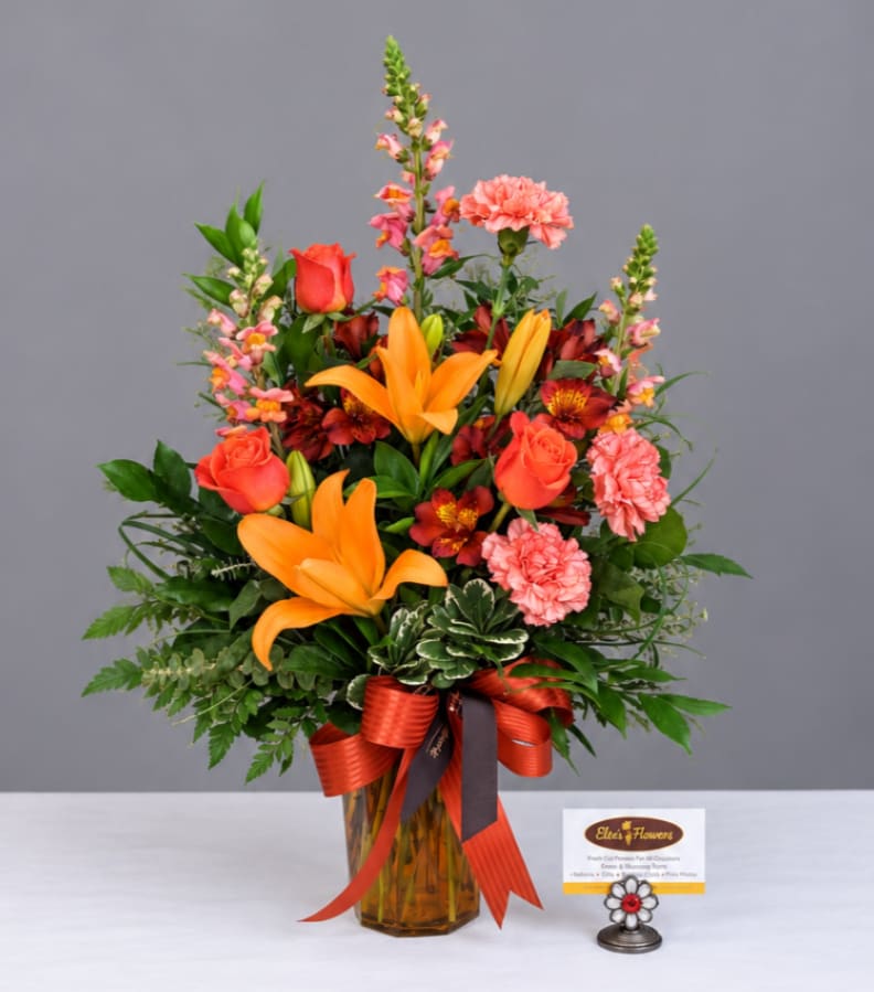 Mixed bouquet in an amber glass vase with orange lilies, roses, and pink carnations