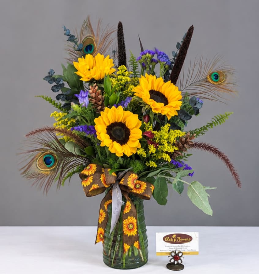 Sunflower bouquet in a green glass vase with peacock feathers and a ribbon