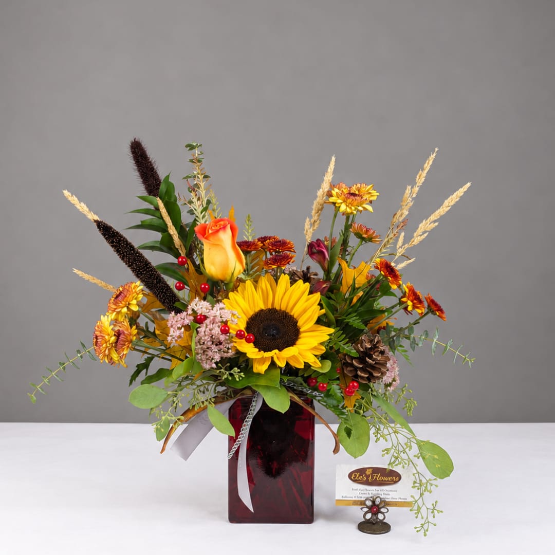 Autumn bouquet with sunflowers, roses, and mums in a red glass vase