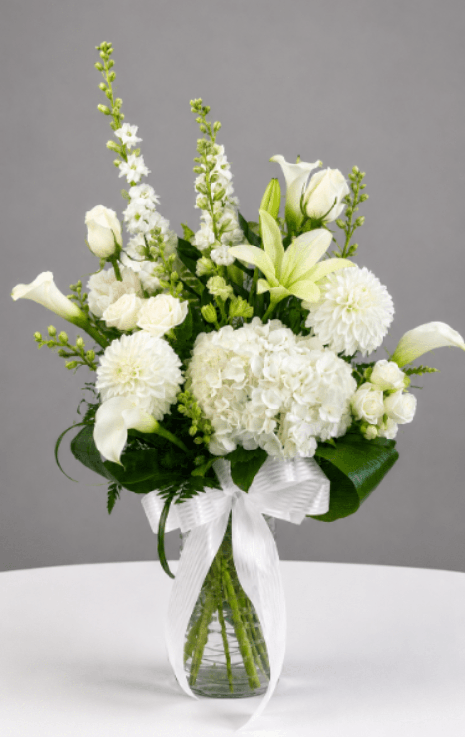 White flowers arranged in a clear glass vase with a white ribbon