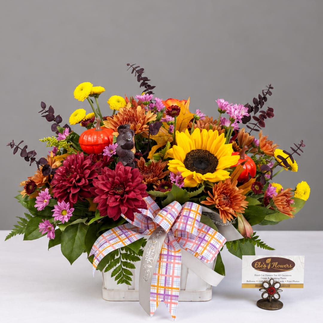 Autumn flower arrangement in a white basket with a plaid ribbon and small pumpkins