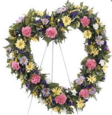 Heart-shaped floral wreath on a stand with pink, yellow, purple, and white flowers