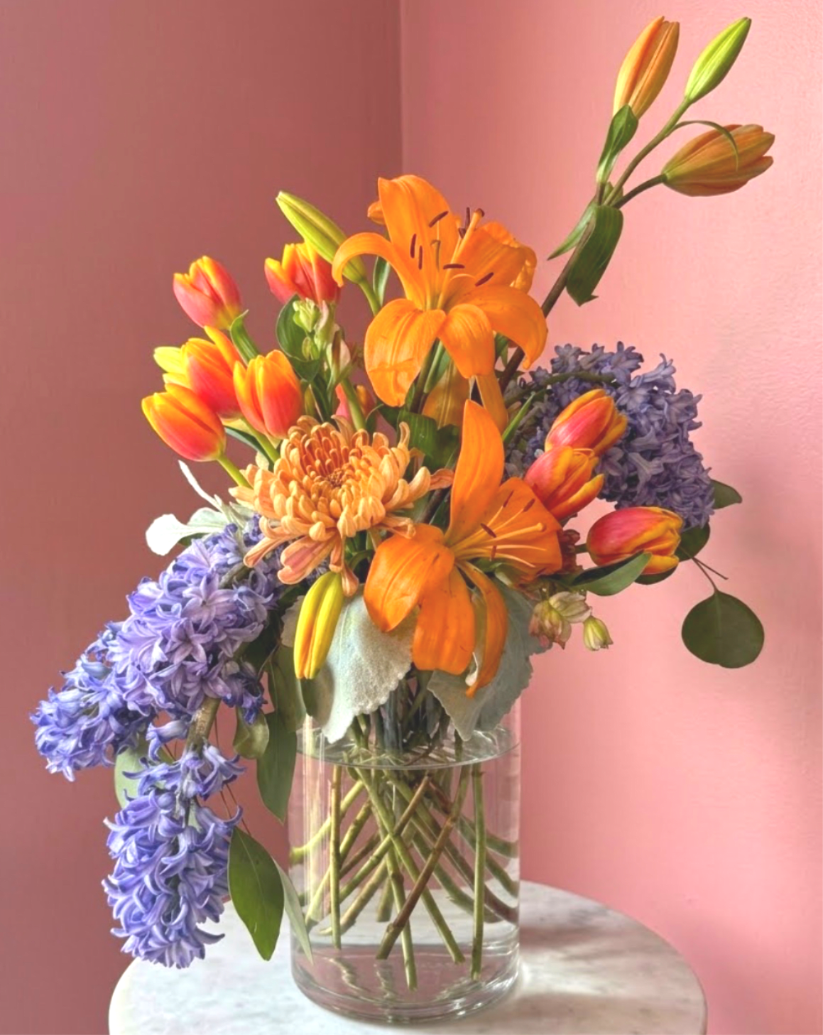 Citrus &amp; Sapphire by Evergreen Elegance : SPRING ONLY  - This vibrant floral arrangement features a warm, autumnal palette of burnt orange, amber, and soft peach, artfully displayed in a classic blue and white chinoiserie porcelain vase.