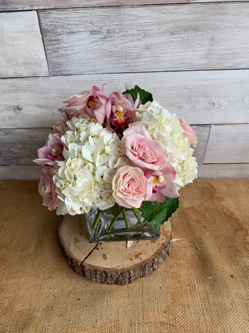Pink and White Delight - This clear cube with white hydrangeas, pink roses and cybidium orchids is delicate for any occasion but specially for baby showers and new parents.