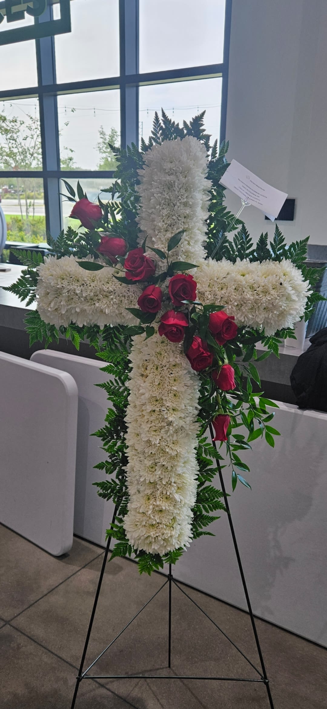 White floral cross on an easel with red roses