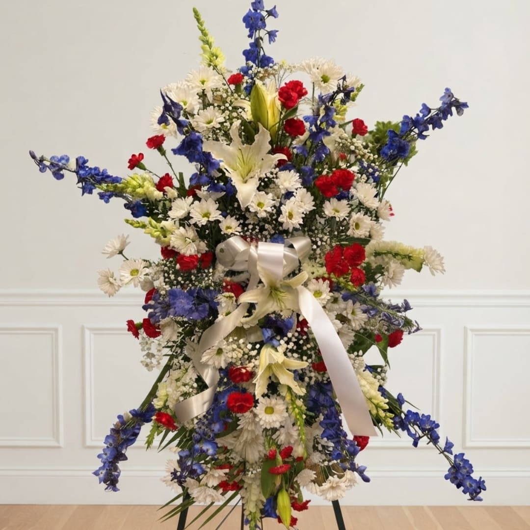 Tall floral standing arrangement with red, white, and blue flowers and a white ribbon