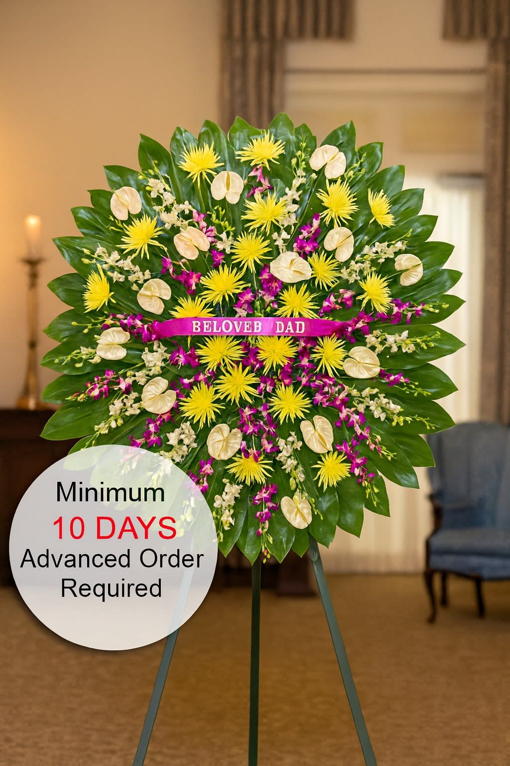 Tall standing sympathy spray with yellow mums, cream tropical blooms and purple orchids on a green leaf fan.