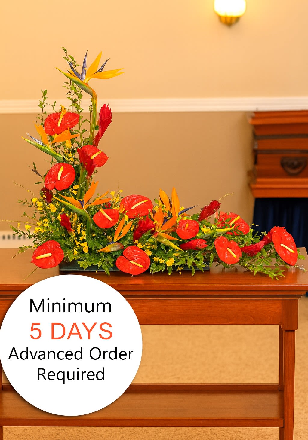 Tropical funeral spray with red and orange flowers arranged low on a wooden table