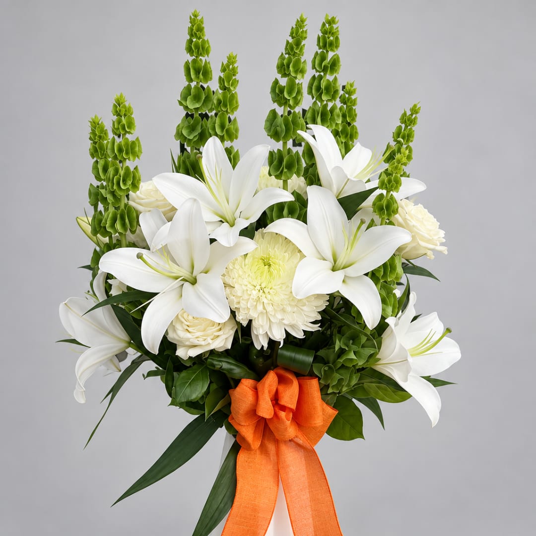 White lilies and cream flowers with tall green spikes, tied with an orange ribbon