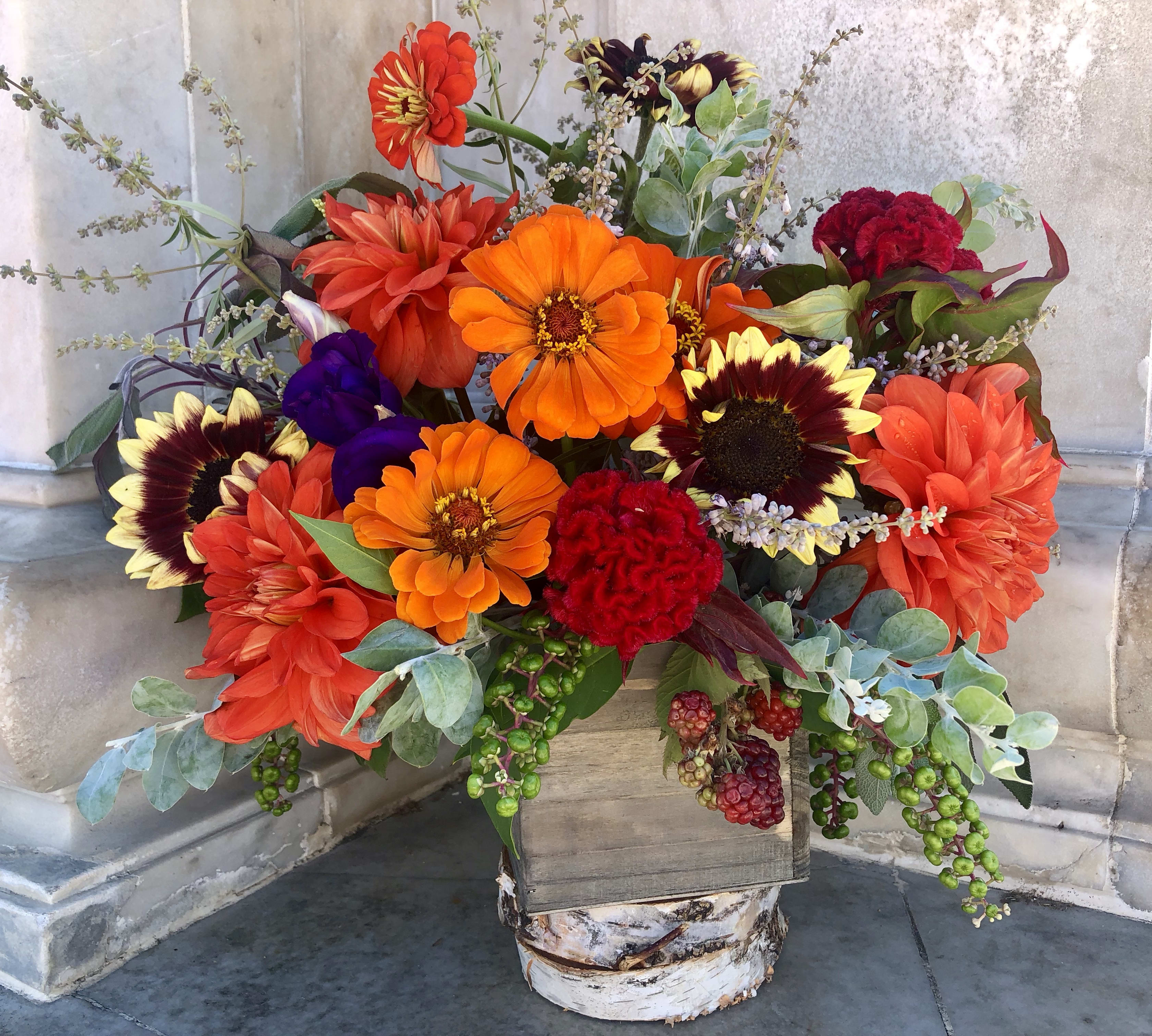 Bright mixed bouquet with orange, red, and purple flowers in a rustic wooden container