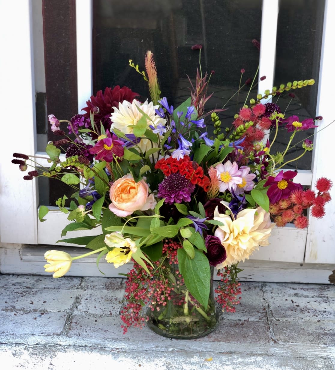 Colorful mixed flower arrangement with roses, dahlias, and tulips in a clear glass vase