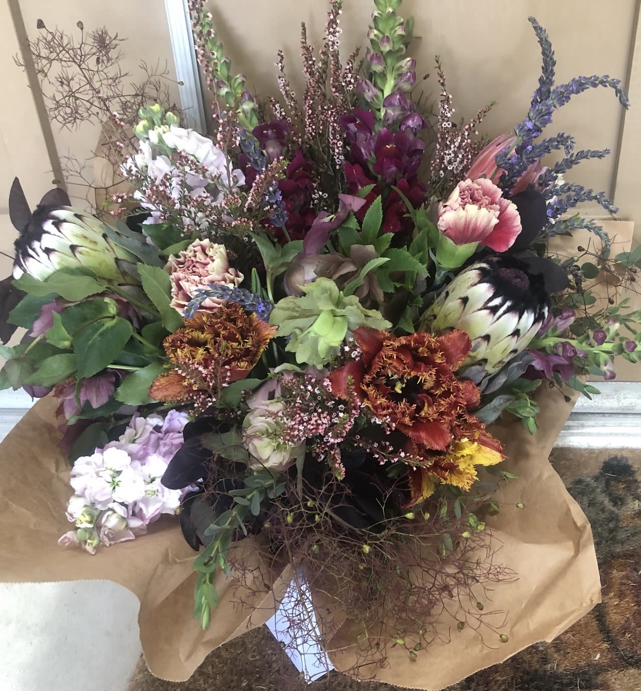 Large mixed bouquet with purple, pink, white, and orange blooms wrapped in brown paper